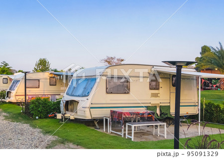 Cozy retro travel trailer Caravan on green grass before sunset near riverside in peaceful countryside. Family vacation travel RV, holiday trip in motorhome. Outdoor and Recreational Vehicles Theme. 95091329