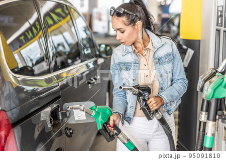 Woman unsure of whether to use petrol or diesel holds both pistols in hands while refuelling at the station 95091810