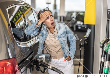 Woman refuelling the tank of her car with diesel looks shocked with mouth open seeing the high price of fuel Woman refuelling the tank of her car with diesel looks shocked with mouth open seeing the high price of fuel 95091811