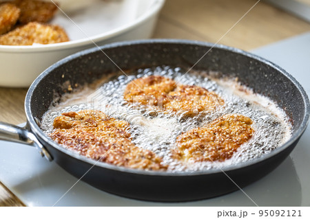 Sizzling hot oil with schnitzel frying in it in a dark pan Sizzling hot oil with schnitzel frying in it in a dark pan 95092121