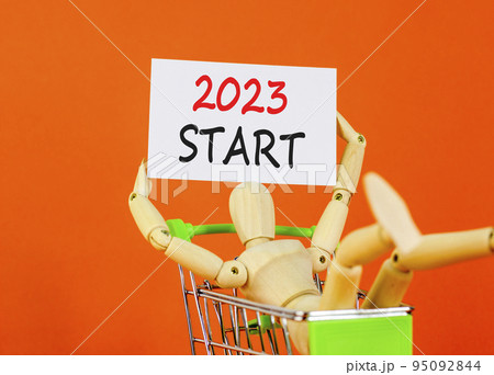 2023 Start symbol. White paper with words 2023 Start, human model in shopcart. Beautiful orange table orange background. Business and 2023 start concept. Copy space. 95092844