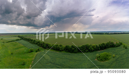 Aerial fly above green fields, stormy cloudscape 95093080