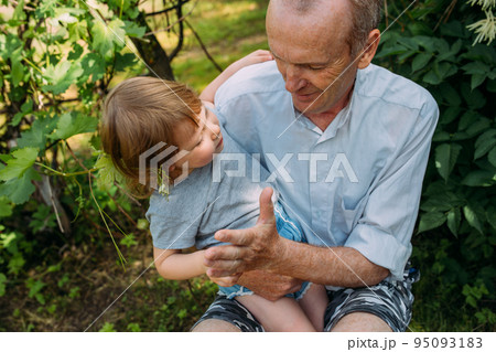 A little girl hugs her grandfather on a walk in the summer outdoors. A little girl hugs her grandfather on a walk in the summer outdoors. 95093183