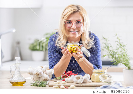 Blonde woman in glasses holds jar of peeled garlic in oil in the kitchen Blonde woman in glasses holds jar of peeled garlic in oil in the kitchen 95096216