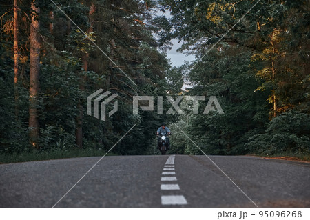 Blurred Motion A young man biker in a helmet quickly rides at high speed on a forest road, in motion 95096268