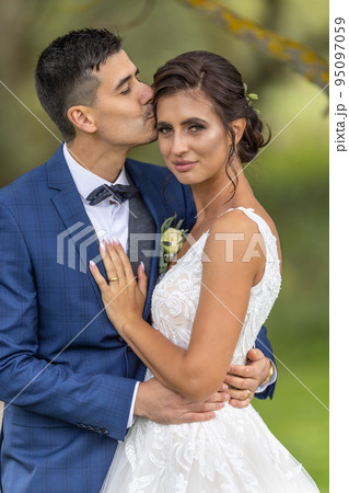 Happy husband kisses his beautiful wife on head during a just married photoshoot Happy husband kisses his beautiful wife on head during a just married photoshoot 95097059