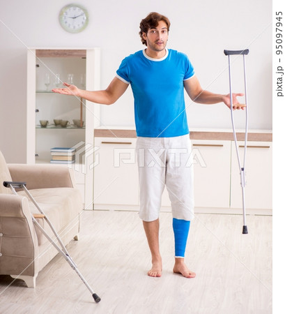 Leg injured young man with crutches at home Leg injured young man with crutches at home 95097945