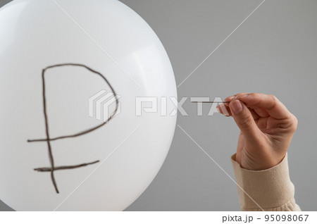 Caucasian woman pops a balloon with a ruble inscription with a needle.  Caucasian woman pops a balloon with a ruble inscription with a needle.  95098067