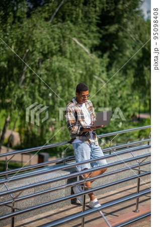 A man with a laptop working outside and looking involved A man with a laptop working outside and looking involved 95098408