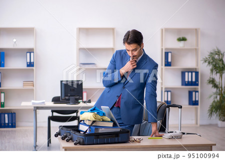 Young male employee preparing for trip at workplace 95100994