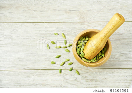 mortar and pestle or bowl with cardamom pods on white wooden kitchen table, top view. mortar and pestle or bowl with cardamom pods on white wooden kitchen table, top view. 95105591