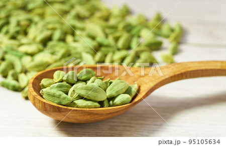 Cardamom pods in a wooden spoon on white wooden kitchen table, selective focus. 95105634