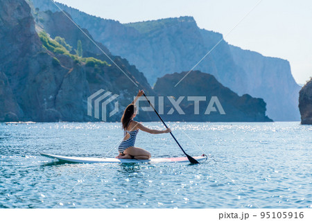 Sporty girl on a glanders surfboard in the sea on a sunny summer day. In a striped swimsuit, it is in the bar. Summer activities by Stortom by the sea Sporty girl on a glanders surfboard in the sea on a sunny summer day. In a striped swimsuit, it is in the bar. Summer activities by Stortom by the sea 95105916