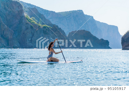 Sporty girl on a glanders surfboard in the sea on a sunny summer day. In a striped swimsuit, it is in the bar. Summer activities by Stortom by the sea Sporty girl on a glanders surfboard in the sea on a sunny summer day. In a striped swimsuit, it is in the bar. Summer activities by Stortom by the sea 95105917