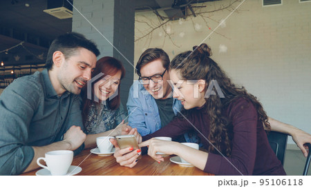 Young happy people are watching smartphone screen discussing photos and laughing during lunch break in cafe. Friendship, modern technology and modern lifestyle concept. Young happy people are watching smartphone screen discussing photos and laughing during lunch break in cafe. Friendship, modern technology and modern lifestyle concept. 95106118