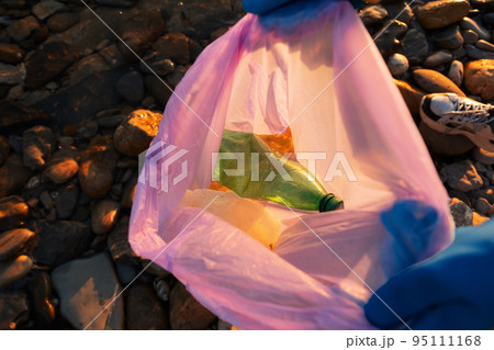 Cleaning from environmental pollution. A volunteer wearing gloves holds an open bag with plastic garbage and bottles. Close-up, top view. The concept of Earth Day and Sustainable Ecology Cleaning from environmental pollution. A volunteer wearing gloves holds an open bag with plastic garbage and bottles. Close-up, top view. The concept of Earth Day and Sustainable Ecology 95111168