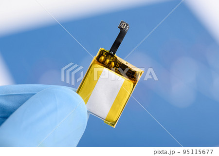 Scientist hold in fingers and show very small rechargeable lithium Li-ion battery with connector  95115677