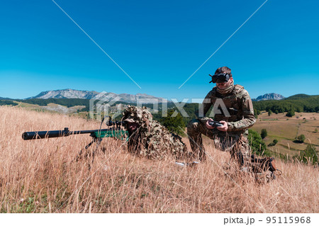 Sniper soldier assisted by an assistant to observe the area to be targeted with modern warfare tactical virtual reality goggles aerial drone military technology. Sniper soldier assisted by an assistant to observe the area to be targeted with modern warfare tactical virtual reality goggles aerial drone military technology. 95115968