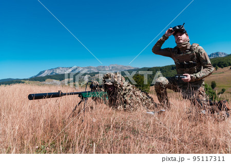Sniper soldier assisted by an assistant to observe the area to be targeted with modern warfare tactical virtual reality goggles aerial drone military technology. 95117311
