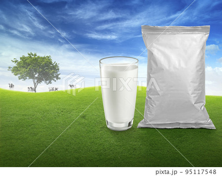 Fresh milk in glass, and foil food packaging, blurred background with cows on the meadow. healthy eating Fresh milk in glass, and foil food packaging, blurred background with cows on the meadow. healthy eating 95117548
