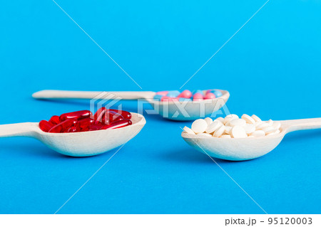 Vitamin capsules in a spoon on a colored background. Pills served as a healthy meal. Red soft gel vitamin supplement capsules on spoon Vitamin capsules in a spoon on a colored background. Pills served as a healthy meal. Red soft gel vitamin supplement capsules on spoon 95120003