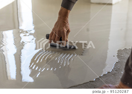 Grey self-leveling screed, new floor layer, man hand. 95120287