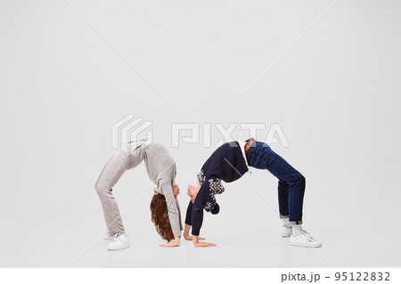 Bridge of understanding. Flexible girl and boy, ballet dancers in warm clothes and hats doing bridges isolated on gray background. 95122832