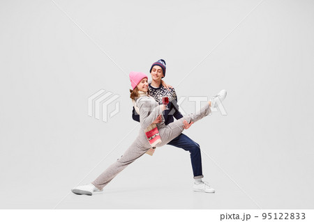 Cute young couple of ballet dancers in warm winter sportswear drinking tea or mulled wine isolated on gray background. Retro, vintage, dance, holidays, party concept 95122833