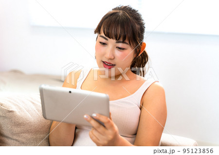 自宅でタブレットを見る若い女性 95123856
