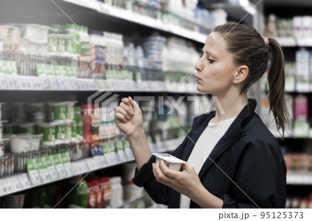 a woman chooses yogurt in a store. Useful food counter selection purchase buyer 95125373