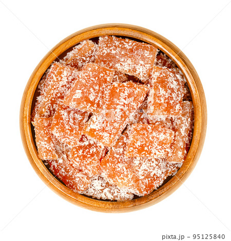 Homemade fruit jelly pieces in a wooden bowl. Sweet fruit gelee dessert with strong flavor, made of pureed fruits, such as quince, mixed with sugar and pectin. The pieces are rolled in coconut shreds. 95125840