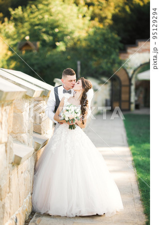 Beautiful bride and groom embracing and kissing on their wedding day 95129294