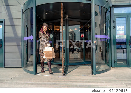 A happy shopaholic girl keeps her bags near the shopping center. A woman near the store is happy with her purchases, holding bags. Dressed in a leopard print dress. Consumer concept. A happy shopaholic girl keeps her bags near the shopping center. A woman near the store is happy with her purchases, holding bags. Dressed in a leopard print dress. Consumer concept. 95129613