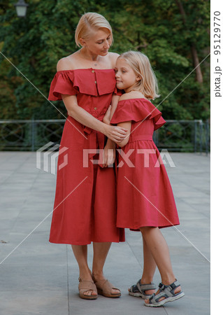 Close up portrait of mother and daughter hugging. Portrait of cheerful mother and daughter. They are wearing red clothes. Happy family blonde mother and daughter. 95129770