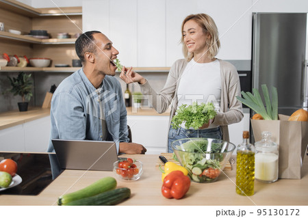 Blond young wife spouses having fun while feeding her husband with lettuce salad Blond young wife spouses having fun while feeding her husband with lettuce salad 95130172