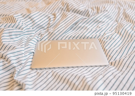 Closed laptop or computer in the morning on a white pillow bed. Lifestyle Concept Closed laptop or computer in the morning on a white pillow bed. Lifestyle Concept 95130419
