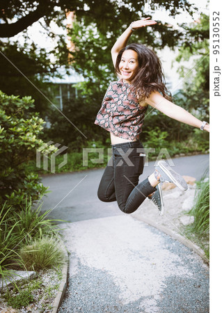 Young happy mixed race Japanese woman in jeans, shirt and sneakers in summer park, jumping and smiling Young happy mixed race Japanese woman in jeans, shirt and sneakers in summer park, jumping and smiling 95130552