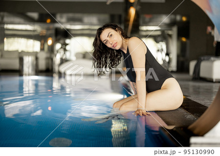 Woman rests by the swimming pool indoors at spa resort 95130990