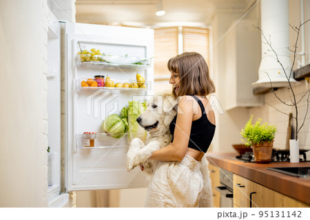 Woman with dog opens fridge filled with healthy food ingredients 95131142
