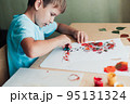 Cute child sitting at desk and making picture from colored dry birch leaves 95131324