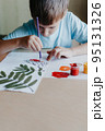 Cute child siting at desk and drawing rowanberries on album sheet with dry rowan leaves 95131326