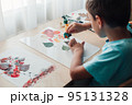 Cute child sitting at desk and making picture from dry birch leaves 95131328