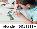 Little child sitting by desk and making picture from dry birch leaves 95131330
