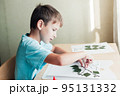 Cute child sitting at desk and making picture from dry birch leaves 95131332