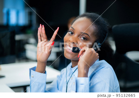 African young woman talking to a client on a headset. Female employee of the call center. 95132665