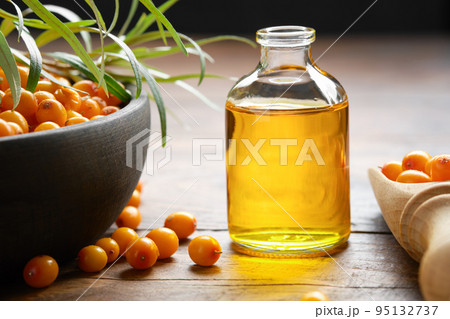 Bottle of sea buckthorn essential oil, bowl of sandthorn berries, wooden scoop of sea buckthorn berries. 95132737