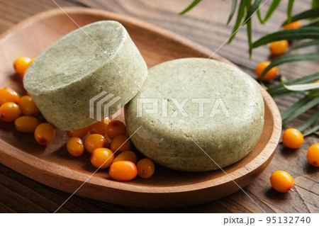 Solid shampoo pieces with sea buckthorn berries extract or homemade natural organic soap bars on wooden soap dish. Ripe sea buckthorn berries on wooden board. Solid shampoo pieces with sea buckthorn berries extract or homemade natural organic soap bars on wooden soap dish. Ripe sea buckthorn berries on wooden board. 95132740