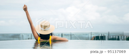 Rear view of asian traveller woman relax at outdoor pool resort sea view on day banner size 95137069