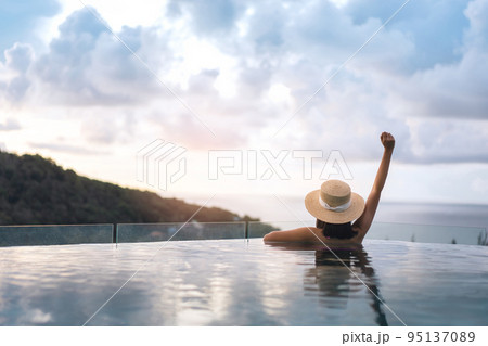 Rear view of asian woman open arm relax at outdoor pool resort sea view on summer sunset 95137089