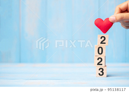 hand holding red heart shape over 2023 wooden cubes on blue table background with copy space for text. Business, Resolution, New Year New Yo hand holding red heart shape over 2023 wooden cubes on blue table background with copy space for text. Business, Resolution, New Year New Yo 95138117